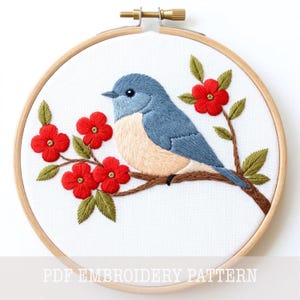 May include: A circular wooden embroidery hoop containing white fabric with a hand-stitched design of a blue bird with a light tan chest perched on a brown branch. The branch features bright red four-petaled flowers and green leaves. PDF EMBROIDERY PATTERN.