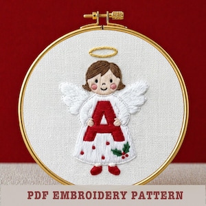 May include: Embroidered angel design in a gold hoop. The angel has brown hair, a halo, and white wings. The red letter "A" is on the angel's dress, which is decorated with red dots and holly. The text "PDF EMBROIDERY PATTERN" is at the bottom.