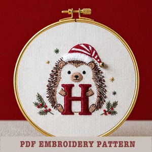 May include: Embroidered hedgehog wearing a Santa hat, holding a red letter "H" in a gold hoop. The design includes sprigs of greenery and stars. Text at the bottom reads "PDF EMBROIDERY PATTERN".
