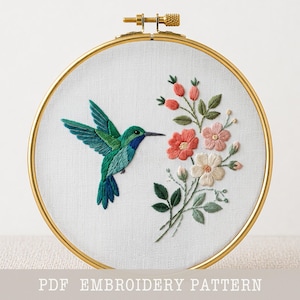 May include: A detailed embroidery hoop featuring a hummingbird and floral design. The hummingbird is depicted with green and blue hues, hovering near a bouquet of pink, red, and white flowers. The text "PDF EMBROIDERY PATTERN" is at the bottom.