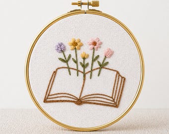 May include: A gold embroidery hoop with a white fabric background. The embroidery features an open book with colorful embroidered flowers sprouting from the pages. The text "PDF EMBROIDERY PATTERN" is at the bottom.