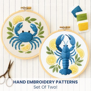 May include: Two hand embroidery patterns in wooden hoops. One features a blue crab with lemon slices and green leaves. The other has a blue lobster with lemon slices and green leaves. The text reads "HAND EMBROIDERY PATTERNS Set Of Two!"