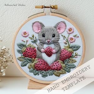Może przedstawiać: Haftowany obręcz z obrazem szarej myszy trzymającej truskawkę, otoczonej różowymi kwiatami i zielonymi liśćmi. Obręcz jest wykonana z drewna i ma podstawkę.