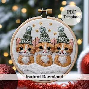 May include: Three orange tabby cats wearing green and white knitted winter hats, embroidered on a white fabric background. The cats are sitting in a row, with their heads tilted slightly to the side. The background is a blurred image of a Christmas tree with lights.