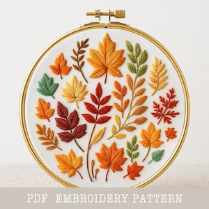 May include: A circular embroidery hoop containing white fabric with hand-stitched autumn leaves in shades of red, orange, yellow, and green. The design features various leaf shapes and textures. The text PDF EMBROIDERY PATTERN is at the bottom.