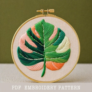 May include: A detailed embroidery of a monstera leaf in a gold hoop. The leaf features shades of green, peach, and cream thread. The text "PDF EMBROIDERY PATTERN" is at the bottom of the image.