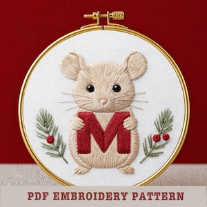 May include: Embroidered hoop art featuring a beige mouse holding a red letter "M". The mouse has black eyes and whiskers. Green sprigs with red berries flank the mouse. The text "PDF EMBROIDERY PATTERN" is at the bottom. The hoop is gold.