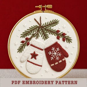May include: Embroidered mittens and evergreen branch design in a gold hoop. One white mitten features a star, the other red mitten has a snowflake. The design includes small white stars and red berries. The text "PDF EMBROIDERY PATTERN" is at the bottom.