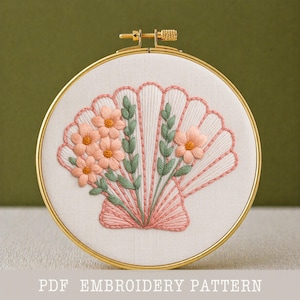 Può includere: Un telaio da ricamo con un motivo floreale. Il design presenta una forma a conchiglia rosa con fiori rosa e foglie verdi. Il testo "PDF EMBROIDERY PATTERN" è in basso.