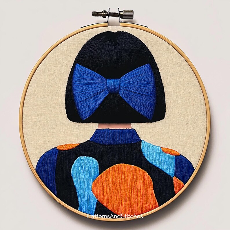 May include: An embroidered hoop art piece featuring a stylized figure with black hair and a large blue bow. The figure wears a black top with blue and orange abstract shapes. The background is a neutral beige fabric.
