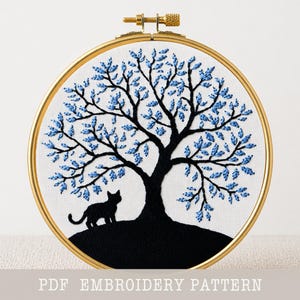 Może przedstawiać: Złoty tamborek z czarnym drzewem z niebieskimi liśćmi i czarną sylwetką kota. Projekt jest umieszczony na białym tle. Tekst "PDF EMBROIDERY PATTERN" znajduje się na dole obrazu.