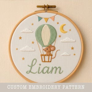 Puede incluir: Arte de aro bordado con un globo aerostático, un ratón, nubes, estrellas y una luna. El nombre "Liam" está bordado en verde. El texto "CUSTOM EMBROIDERY PATTERN" está en la parte inferior.