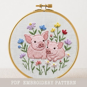Op de afbeelding: Geborduurd kunstwerk met twee roze varkens omringd door kleurrijke bloemen in een gouden hoepel. De borduursels bevatten blauwe, paarse, gele en rode bloemen. De tekst "PDF EMBROIDERY PATTERN" staat onderaan.