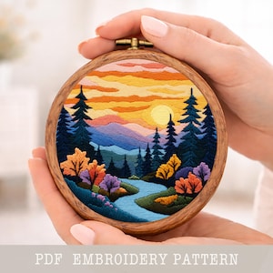 Peut inclure: Un cercle à broder en bois avec un paysage coloré. Le motif représente un coucher de soleil, des montagnes, des arbres et une rivière. Le texte "PDF EMBROIDERY PATTERN" est visible en bas.