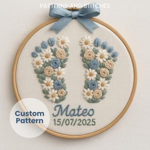 May include: Embroidered baby feet design in a wooden hoop. The design features blue, white, and tan flowers and leaves, with the name "Mateo" and the date "15/07/2025" embroidered in blue thread. A blue ribbon bow is attached at the top.