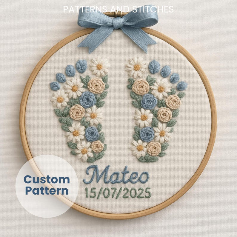 May include: Embroidered baby feet design in a wooden hoop. The design features blue, white, and tan flowers and leaves, with the name "Mateo" and the date "15/07/2025" embroidered in blue thread. A blue ribbon bow is attached at the top.
