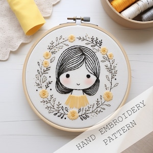 Op de afbeelding: Handborduurpatroon met een meisje met zwart haar en een gele jurk omringd door een krans van gele bloemen en bladeren. Het patroon is in een houten borduurring.