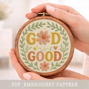 Puede incluir: Un bastidor de bordado redondo con las palabras "GOD is GOOD" bordadas en hilo amarillo, naranja y melocotón. El diseño incluye detalles florales y de hojas. El bastidor de madera está sostenido en las manos de una persona.