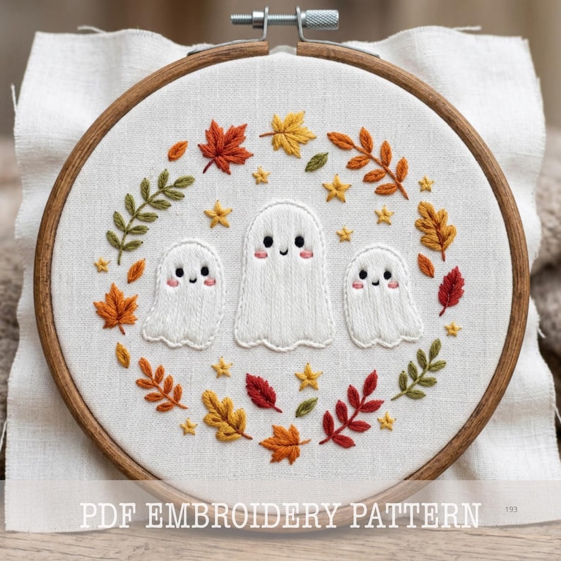 May include: A circular wooden embroidery hoop containing white fabric with a hand-stitched design of three white ghosts surrounded by a wreath of colorful autumn leaves and small yellow stars. The text PDF EMBROIDERY PATTERN is visible.