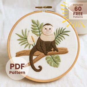 May include: Embroidered hoop art showing a brown monkey with a white face and collar, sitting on a brown branch. Green leaves and a white flower surround the monkey. The text "PDF Pattern" and "Includes 60 FREE Patterns" are also visible.