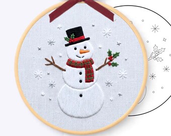 May include: A hand embroidery pattern featuring a snowman wearing a black top hat with red ribbon and holly, an orange carrot nose, and a red and green plaid scarf. The snowman is surrounded by white embroidered snowflakes on fabric in a 20 cm hoop.