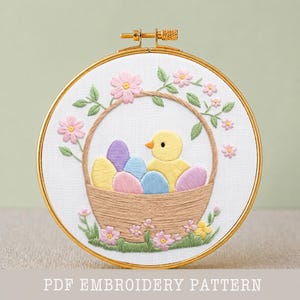May include: Embroidered Easter design in a gold hoop. A yellow chick sits in a woven basket filled with pastel colored eggs. Pink flowers and green leaves surround the basket. The text "PDF EMBROIDERY PATTERN" is at the bottom.