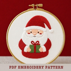 May include: Embroidered Santa Claus design in a gold hoop. Santa wears a red hat and suit, holding a green gift with a red bow. The text "PDF EMBROIDERY PATTERN" is at the bottom. The embroidery is on white fabric.