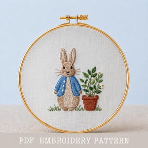 May include: An embroidery hoop with a Peter Rabbit design. The design features a brown rabbit wearing a blue jacket, standing next to a potted plant. The text "PDF EMBROIDERY PATTERN" is at the bottom.