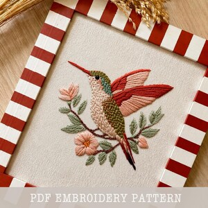 May include: Embroidered hummingbird art piece. The bird features a mix of pink, green, and red thread, perched on a branch with pink flowers and green leaves. The artwork is framed in a red and white striped wooden frame. The text "PDF EMBROIDERY PATTERN" is at the bottom.