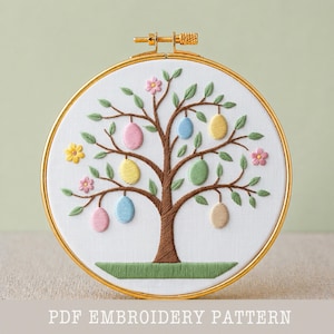 Può includere: Ricamo di un albero di Pasqua in un cerchio dorato. L'albero presenta uova di Pasqua dai colori pastello, foglie verdi e fiori rosa e gialli. Il testo "PDF EMBROIDERY PATTERN" è in basso.