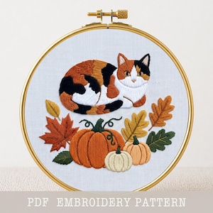 Könnte beinhalten: Stickrahmen mit einer dreifarbigen Katze, umgeben von Herbstblättern und Kürbissen. Die Katze hat orangefarbenes, braunes und schwarzes Fell. Die Kürbisse sind orange und cremefarben. Der Text "PDF EMBROIDERY PATTERN" befindet sich unten.