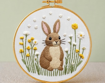 Op de afbeelding: Geborduurde borduurring met een bruin konijn omringd door gele en witte bloemen. Het ontwerp staat op witte stof, omlijst door een goudkleurige ring. De tekst onderaan luidt "PDF EMBROIDERY PATTERN".