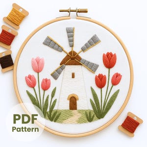 May include: Embroidered windmill and tulip design in a wooden hoop. The white windmill has gray blades and a brown roof. Red and pink tulips with green leaves surround the windmill. The text "PDF Pattern" is in the lower left corner. Spools of thread are in the upper left and lower right.