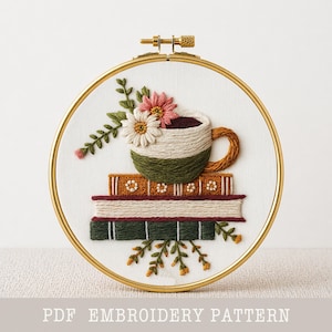 May include: Embroidered hoop art featuring a coffee cup with flowers atop a stack of books. The cup is beige and green, with a brown handle. The books are in shades of brown and green. The text "PDF EMBROIDERY PATTERN" is at the bottom.