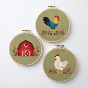 May include: Three embroidered hoops with farmyard designs. One shows a red barn, another a rooster with blue and yellow plumage, and the third a white hen. All are set against a green background with floral accents, framed in wooden hoops.