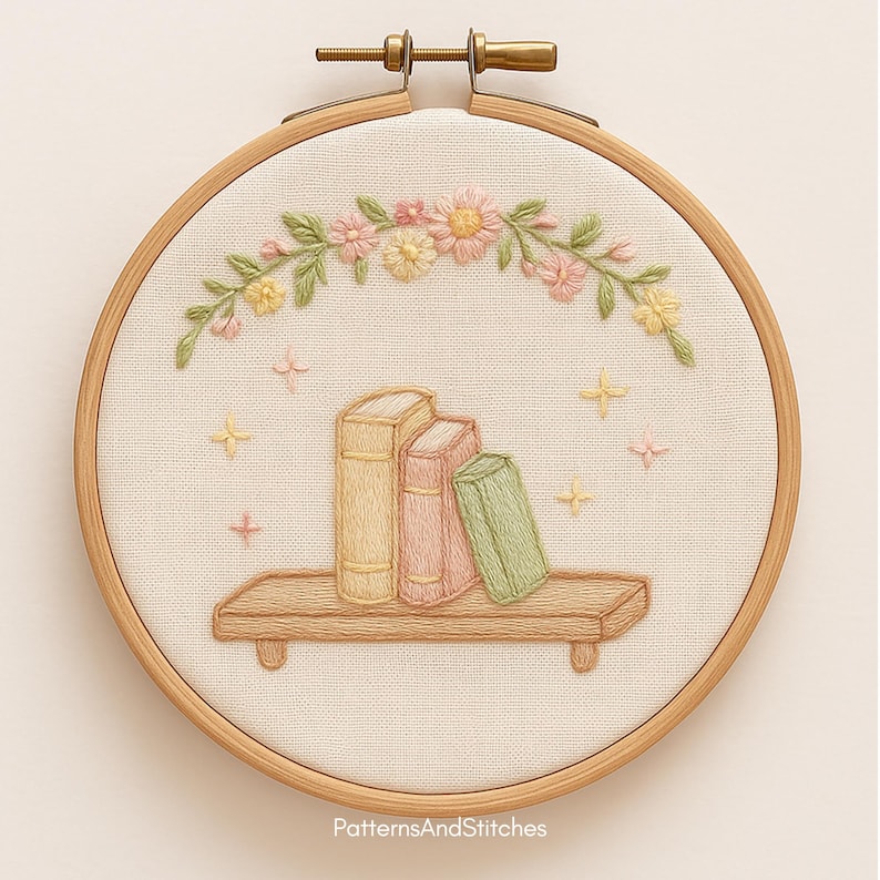 Puede incluir: Arte bordado en bastidor que muestra una estanter&iacute;a con tres libros en colores pastel. Una estanter&iacute;a de madera sostiene los libros, con un arco floral encima. El fondo es de tela beige claro, y el bastidor es de madera. El texto "PatternsAndStitches" est&aacute; en la parte inferior.