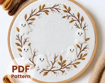 May include: Embroidered hoop art featuring a white fabric with a stitched design of smiling ghost figures and autumn leaves. The text "PDF Pattern" is visible. The wooden hoop is surrounded by brown and yellow embroidery floss.