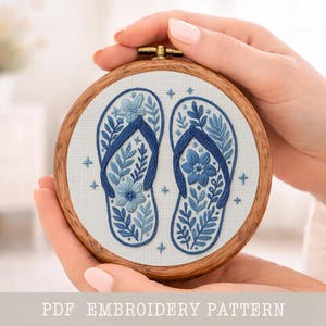 以下が含まれることがあります： 青いビーチサンダル2足が刺繍されたアート作品。花と葉のデザインが施され、木製のフレームに収められています。「PDF EMBROIDERY PATTERN」の文字が画像の下部にあります。