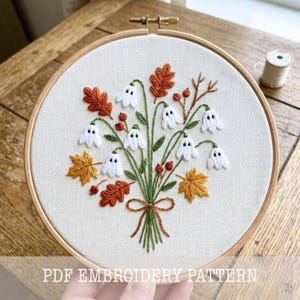 Peut inclure: Un tambour à broder circulaire en bois contenant un tissu blanc avec un bouquet brodé à la main de feuilles d'automne, de baies rouges et de petits fantômes blancs. Les tiges sont nouées par un nœud en fil marron. Texte PDF EMBROIDERY PATTERN.