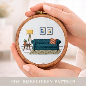 Puede incluir: Un bastidor de bordado detallado con una escena de sala de estar en miniatura. El diseño incluye un sofá capitoné de color verde azulado, una lámpara de pie y arte abstracto. El texto "PDF EMBROIDERY PATTERN" está en la parte inferior.