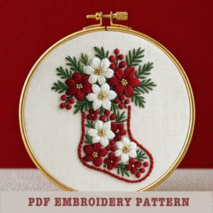 May include: Embroidered Christmas stocking design in a gold hoop. The stocking is filled with red and white flowers, green leaves, and red berries. The text "PDF EMBROIDERY PATTERN" is at the bottom.