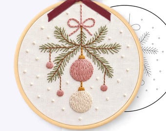 Könnte beinhalten: Ein Handstickmuster-PDF in einem 20 cm großen Holzrahmen. Der Stoff zeigt grüne Tannenzweige, rosa und cremefarbene Ornamente sowie eine rosa Schleife. Oben ist ein dunkelrotes Samtband befestigt.