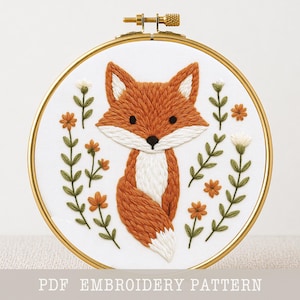 May include: An embroidered fox design in a gold hoop. The fox is a warm orange colour with white and brown details, set against a white background. Green leaves and orange flowers surround the fox. The text "PDF EMBROIDERY PATTERN" is at the bottom.
