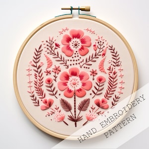 Pode incluir: Um padrão de bordado à mão com um desenho floral com duas grandes flores cor-de-rosa, folhas e flores cor-de-rosa menores. O padrão está em um aro de bordado de madeira. O texto "HAND EMBROIDERY PATTERN" está na parte inferior da imagem.