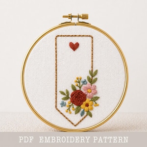 May include: Embroidered floral design in a gold hoop. The design features a red heart, a brown stitched border, and a bouquet of flowers in shades of red, pink, yellow, and blue. The text "PDF EMBROIDERY PATTERN" is at the bottom.