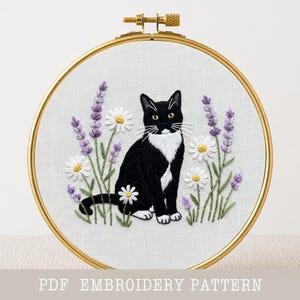 May include: Embroidered cat design in a gold hoop. A black and white cat sits amongst embroidered lavender and daisies. The text "PDF EMBROIDERY PATTERN" is at the bottom of the image.