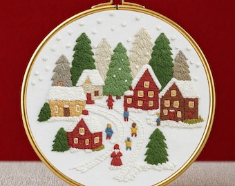 May include: An embroidered winter village scene in a gold hoop. The design features snow-covered houses, evergreen trees, and figures walking along a snowy path. The text "PDF EMBROIDERY PATTERN" is at the bottom.