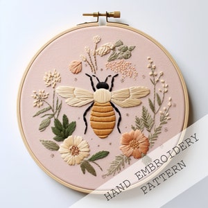 May include: A hand embroidery pattern featuring a bee surrounded by flowers in shades of pink, yellow, and green. The pattern is displayed in a wooden embroidery hoop. The text "HAND EMBROIDERY PATTERN" is displayed below the hoop.
