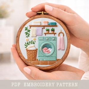 May include: A detailed embroidery hoop featuring a laundry room scene. The design includes a washing machine, towels, plants, and a laundry basket. The text "PDF EMBROIDERY PATTERN" is at the bottom.