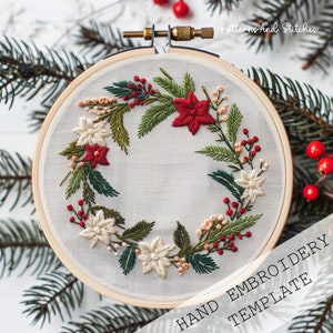 Puede incluir: Un aro de bordado blanco con un diseño de corona navideña cosido a mano. La corona está hecha de hojas verdes, bayas rojas, flores blancas y flores de poinsettia rojas. El texto "HAND EMBROIDERY TEMPLATE" está impreso debajo del aro.